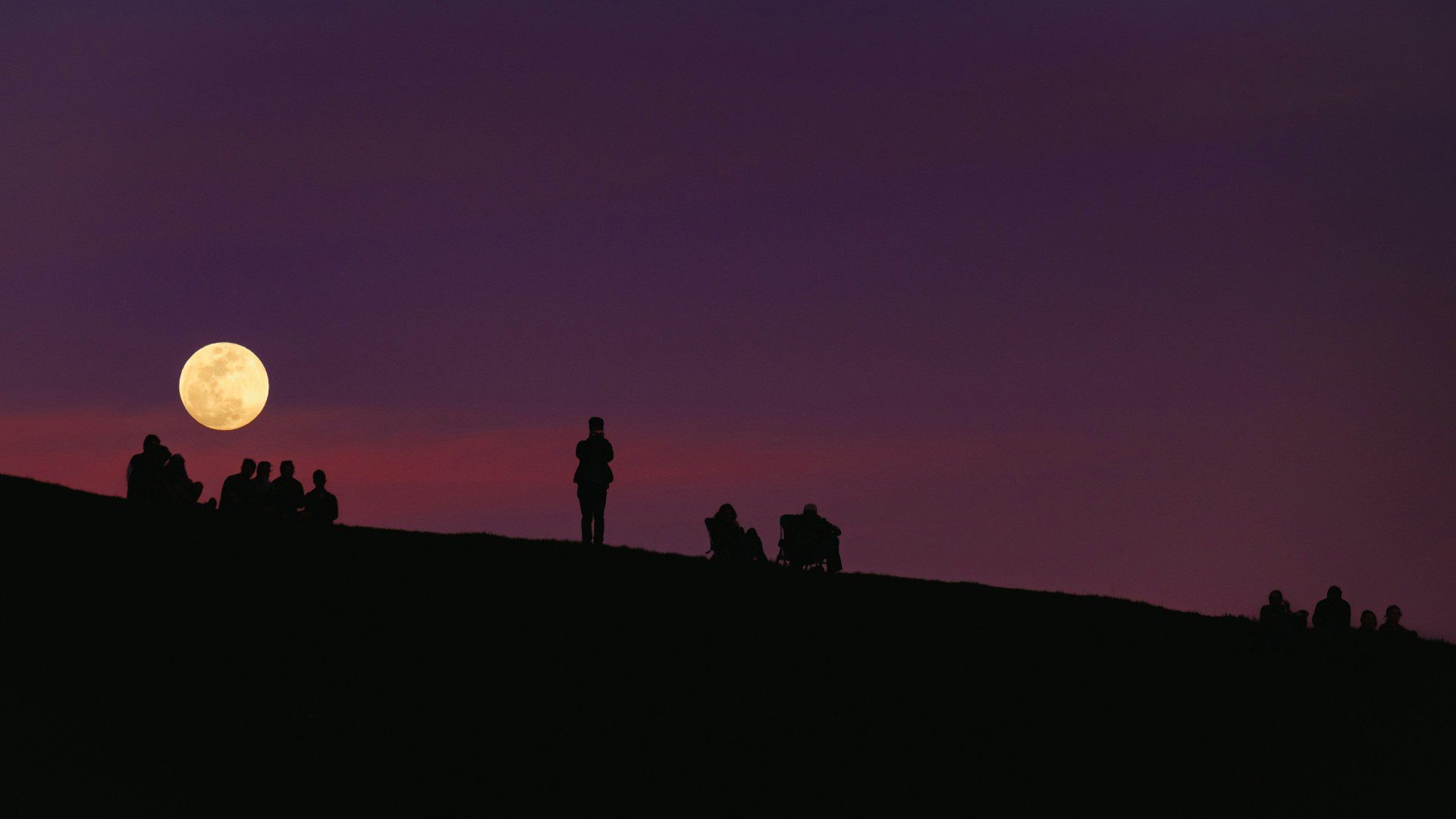 People on hillside watching moon rise